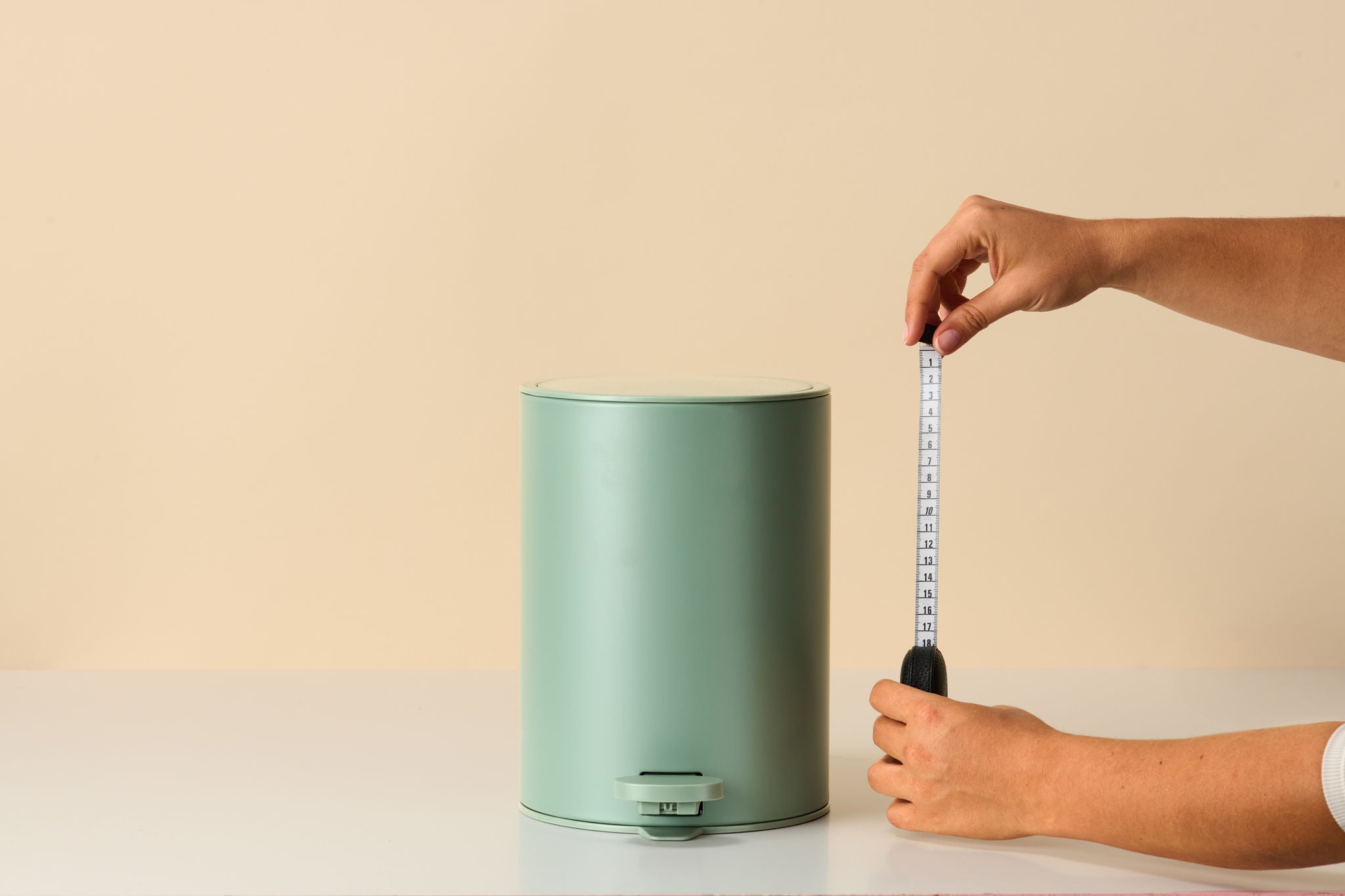 Hände messen mit Maßband Mülleimer-Höhe aus