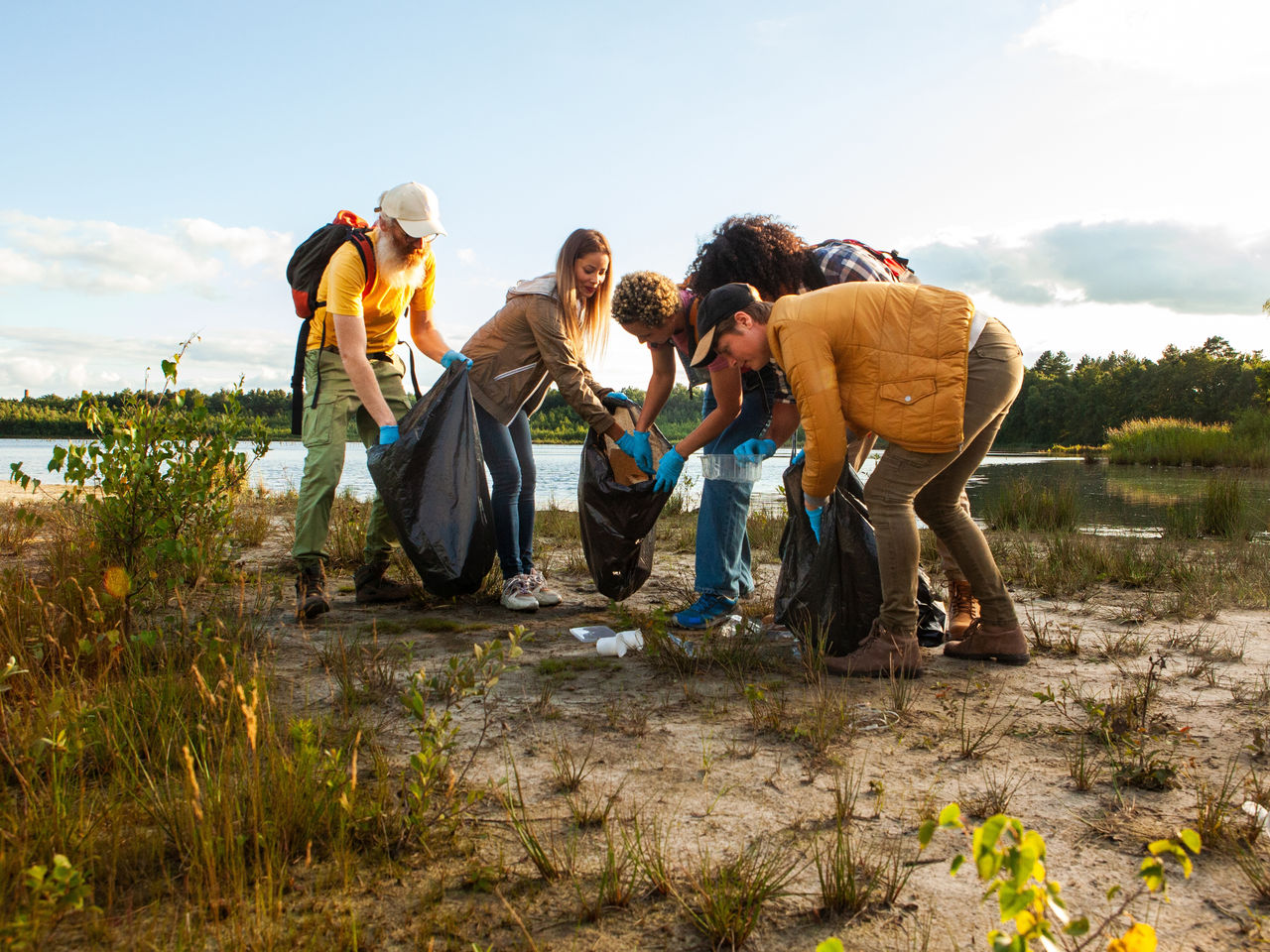 Gruppe von fünf Menschen sammelt gemeinsam Müll in einer Landschaft